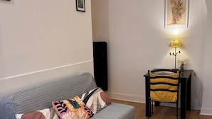 Un salón con un sofá gris, una mesita con un libro, una lámpara amarilla y un sillón con cojín amarillo.