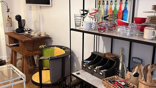 Una cocina con una mesa de madera, una cafetera y una estantería con diversos utensilios.