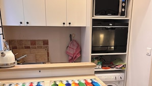 Una cocina con armarios blancos, microondas, estufa, lavamanos y lavadora.