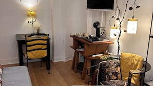 Una sala de estar acogedora con un sofá, una mesa de centro de vidrio, un escritorio con una lámpara, un televisor y una planta decorativa.
