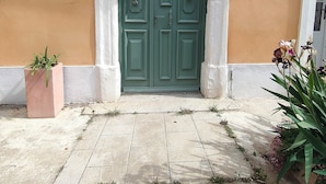 A green door with decorative glass panels, flanked by two wall-mounted lanterns, set against a peach-colored wall with a white trim. - Appartement Dans Maison de Maître au Cœur des Corbières, à 9 min de Fontfroide (Saint-André-de-Roquelongue)