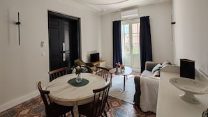 A dining area with a round table, chairs, and a vase of flowers. There is a sofa and a television in the background. - Appartement Dans Maison de Maître au Cœur des Corbières, à 9 min de Fontfroide (Saint-André-de-Roquelongue)