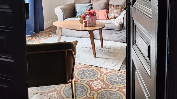 A room with a patterned floor, a sofa with cushions, a coffee table with decorative items, and a door with a dark frame. - Appartement Dans Maison de Maître au Cœur des Corbières, à 9 min de Fontfroide (Saint-André-de-Roquelongue)
