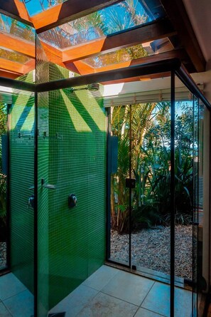 Un área de ducha moderna con paredes de vidrio, revestimiento de azulejos verdes y vistas a plantas tropicales.