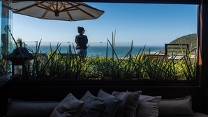 A room with a large window overlooking the ocean, a beach, and a mountain. - Morada Prainha (Garopaba)