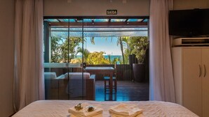 A hotel room with a bed, a TV, and a view of the beach. - Morada Prainha (Garopaba)