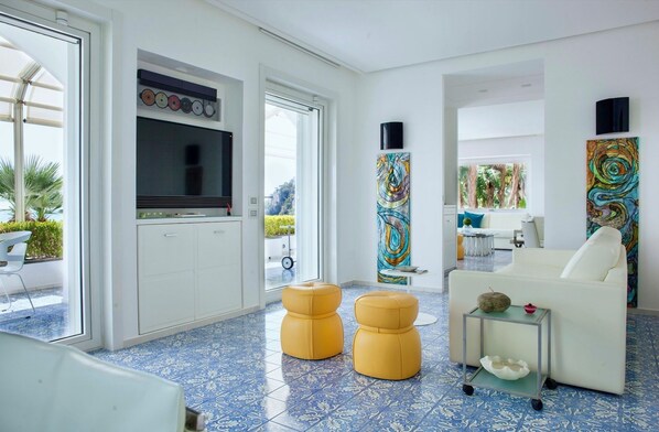 A modern living room with a TV, two yellow ottomans, a white sofa, and abstract paintings.