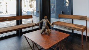Un interior modern amb dues banquetes de fusta i una taula de metall, finestres grans i un sostre de formigó.