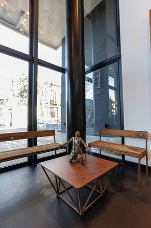 A modern interior with two wooden benches and a metal table, large windows, and a concrete ceiling. - Howard Johnson Undici Republica de La Boca (Buenos Aires)