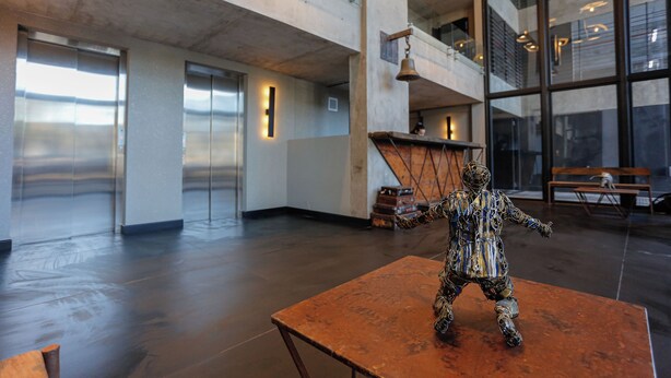 Un vestíbulo amplio con una gran escultura sobre una mesa, ascensores y un techo alto con luces colgantes.