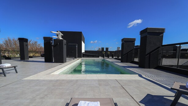 Zona d'una piscina al terrat amb gandules, una estàtua i un cel blau clar.