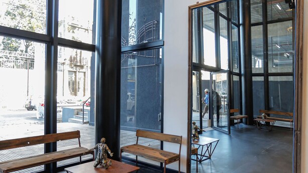A modern interior with large windows, wooden benches, and a small table. - Howard Johnson Undici Republica de La Boca (Buenos Aires)