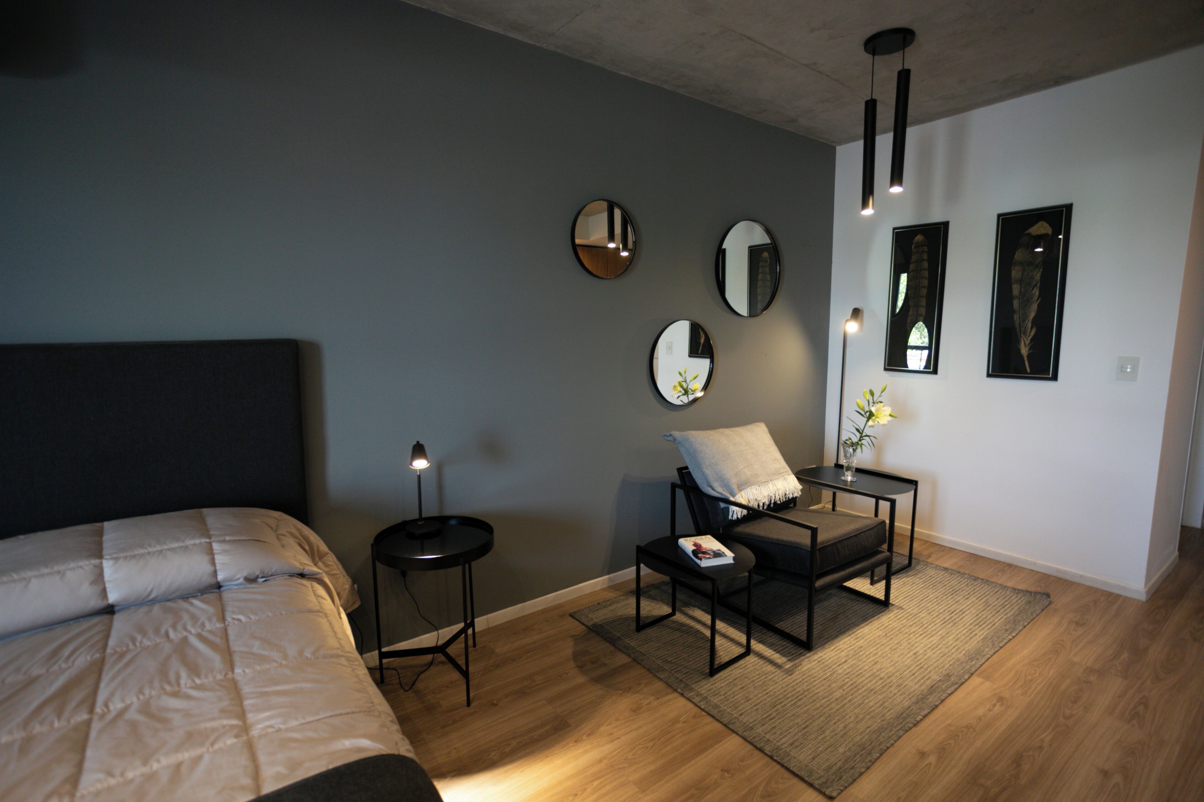 A modern bedroom with a bed, bedside table, chair, and wall-mounted mirrors.