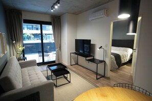 Une chambre d’hôtel moderne avec un canapé, une petite table, un téléviseur posé sur un meuble, une table de chevet avec une lampe et un lit.