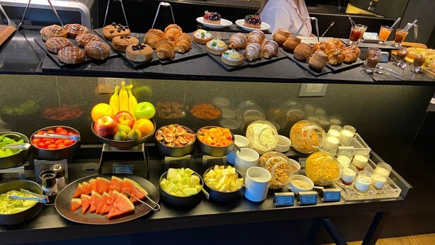 Un bufé con diversas opciones de comida, incluyendo pasteles, frutas y bebidas.