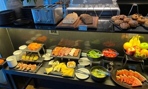 Un buffet proposant une variété d’aliments, notamment du pain, des pâtisseries, de la viande, du fromage et des fruits.