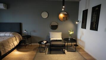 Un dormitorio moderno con cama, mesitas de noche, un sillón de lectura, una pequeña mesa con un florero y espejos en la pared.