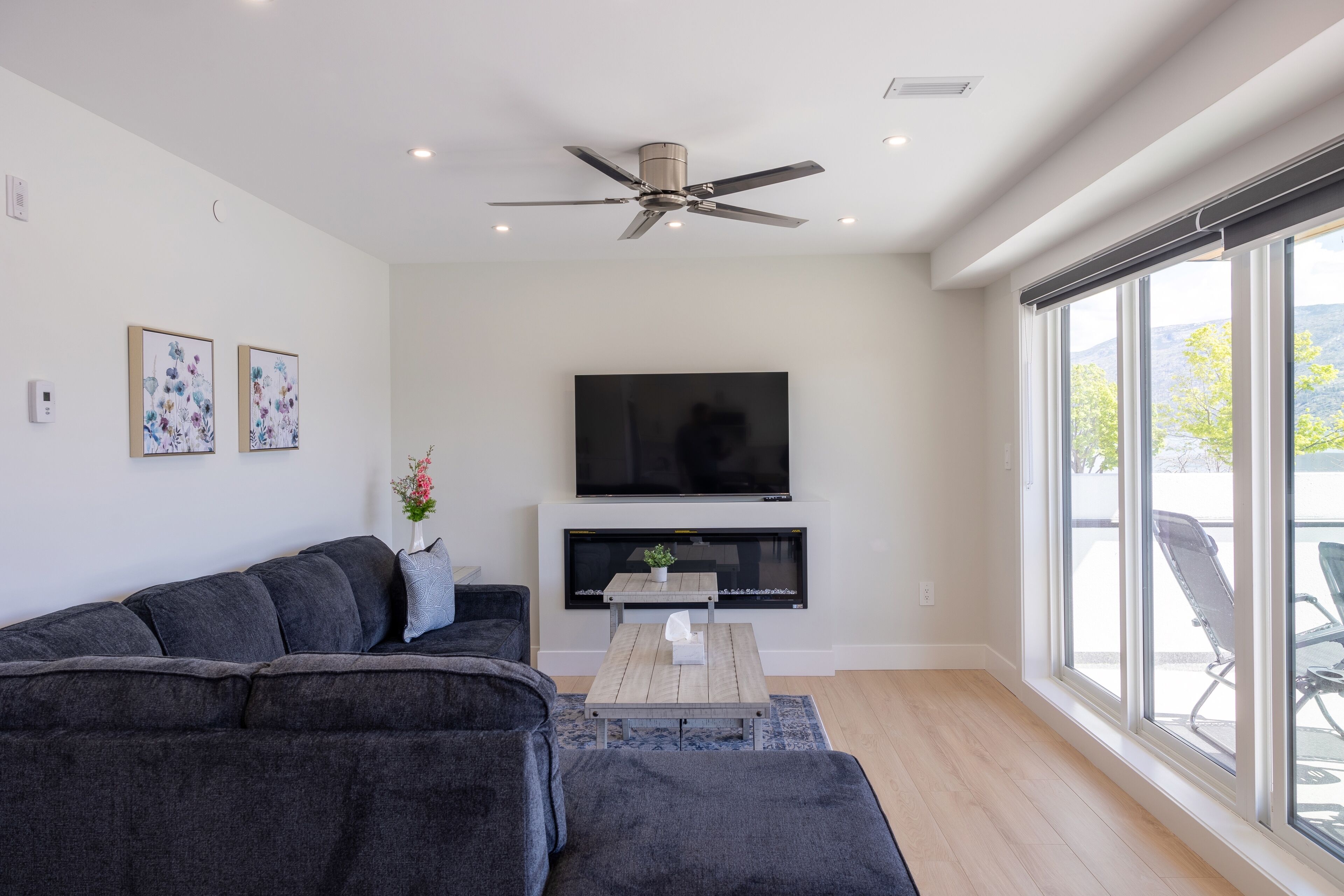 Un salon moderne avec un canapé gris foncé, un téléviseur à écran plat et un ventilateur de plafond.