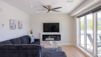 Un salon moderne avec un canapé gris foncé, un téléviseur à écran plat et un ventilateur de plafond.