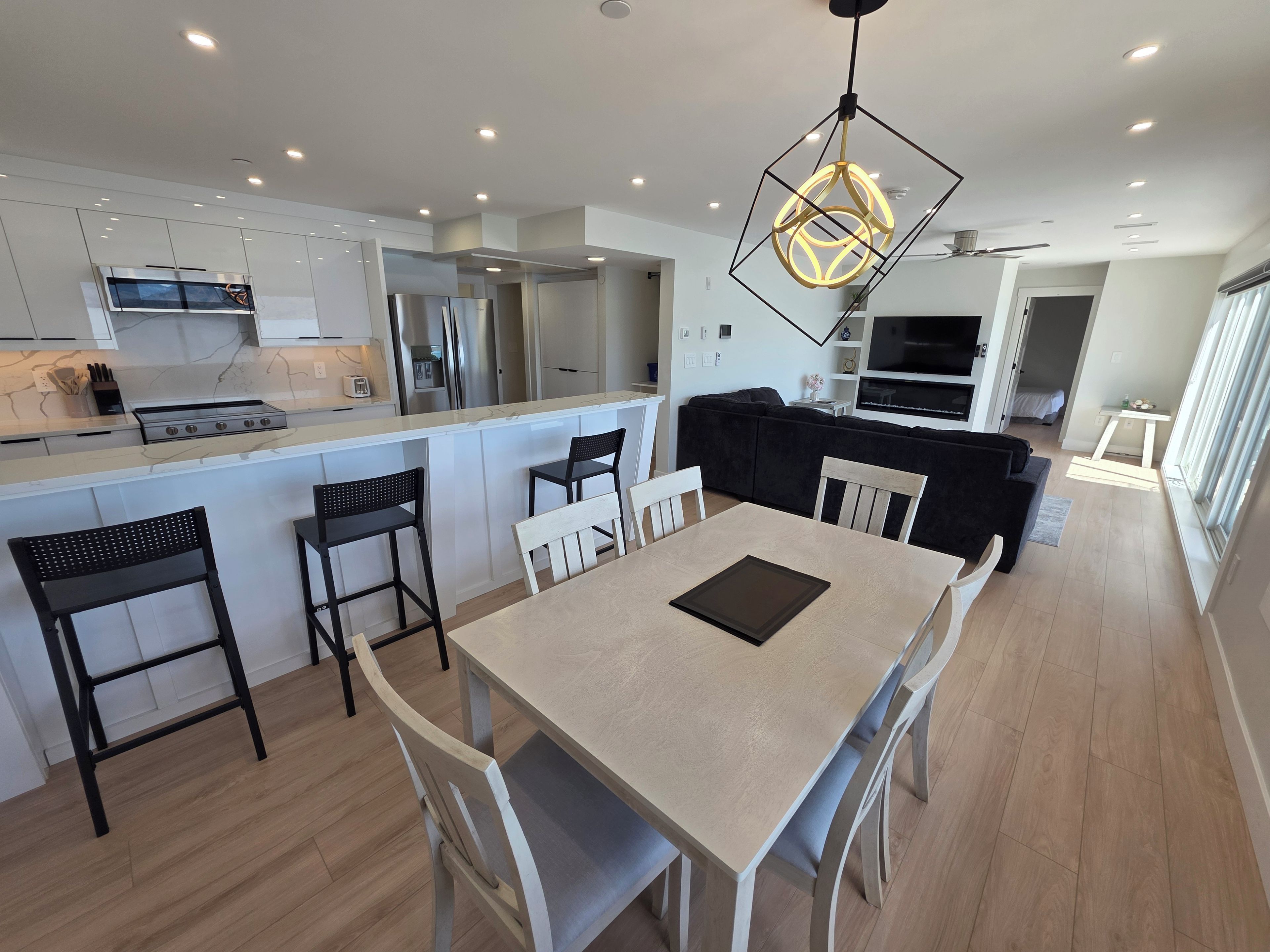 Una cocina moderna con una isla central, taburetes negros, una mesa de comedor con sillas y una lámpara colgante.