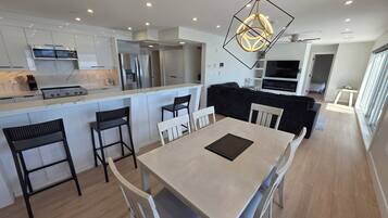 Una cocina moderna con una isla central, taburetes negros, una mesa de comedor con sillas y una lámpara colgante.