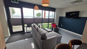A modern office space with a sofa, chairs, a TV, and large windows overlooking a body of water.
