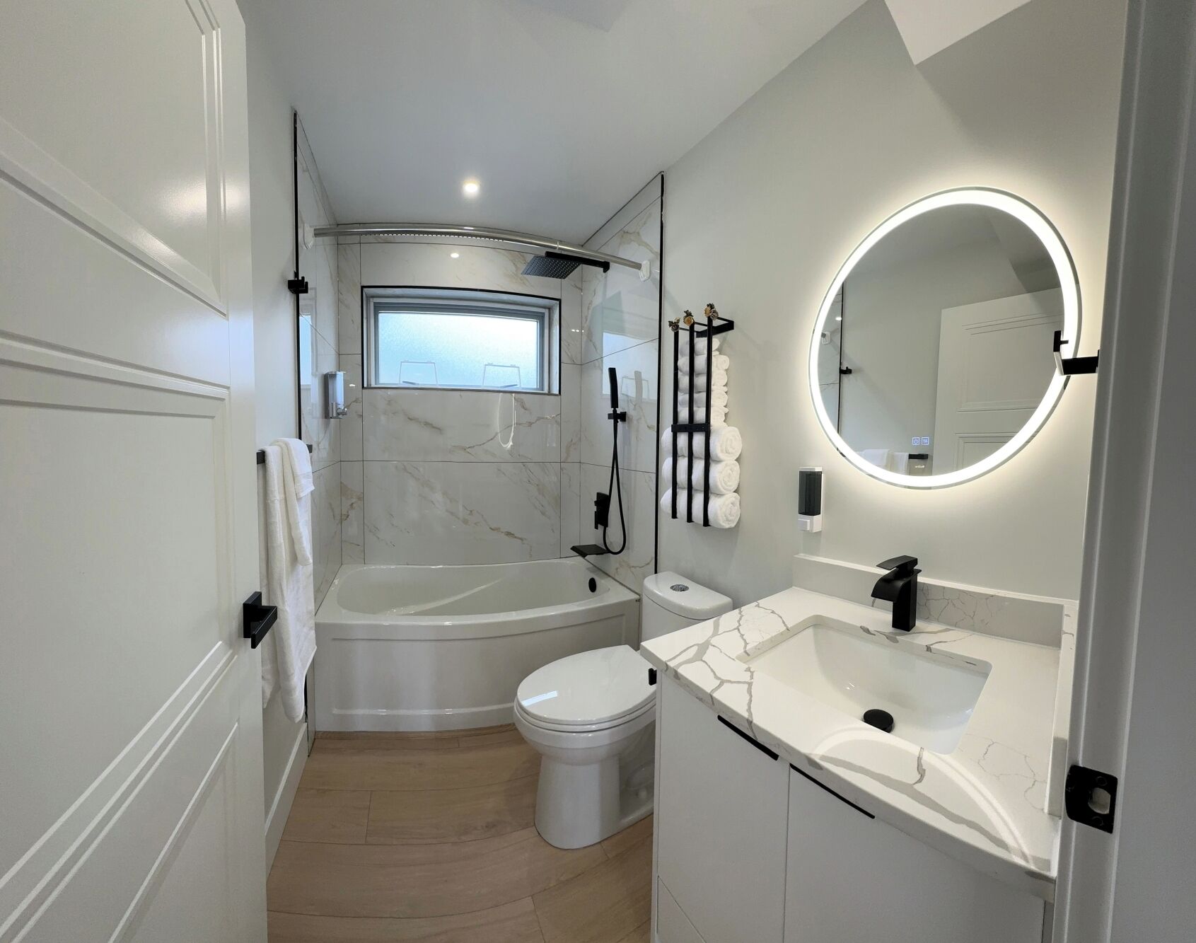 Un baño moderno con bañera, inodoro y lavamanos, que cuenta con un ventanal y un espejo redondo.