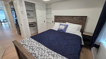 Un dormitorio con cama, cabecero de madera, armario con espacio para colgar y mesita de noche.