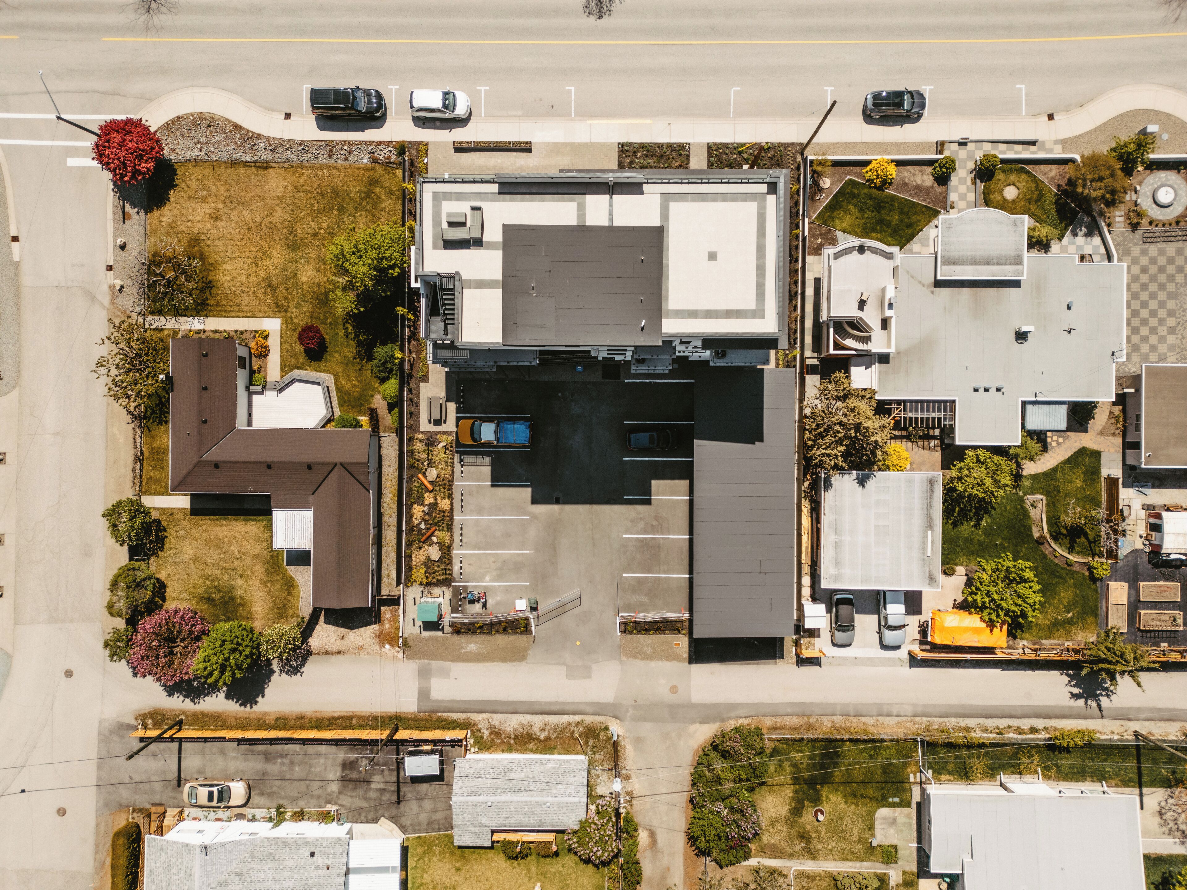 An aerial view of a commercial building with a parking lot, adjacent smaller buildings, and surrounding greenery.