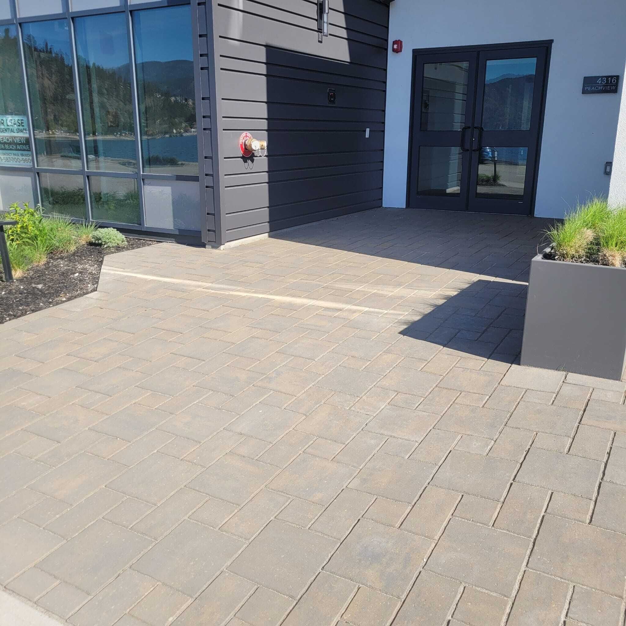 Un edificio moderno con un área de entrada pavimentada, fachada de vidrio y una puerta con señal numérica.