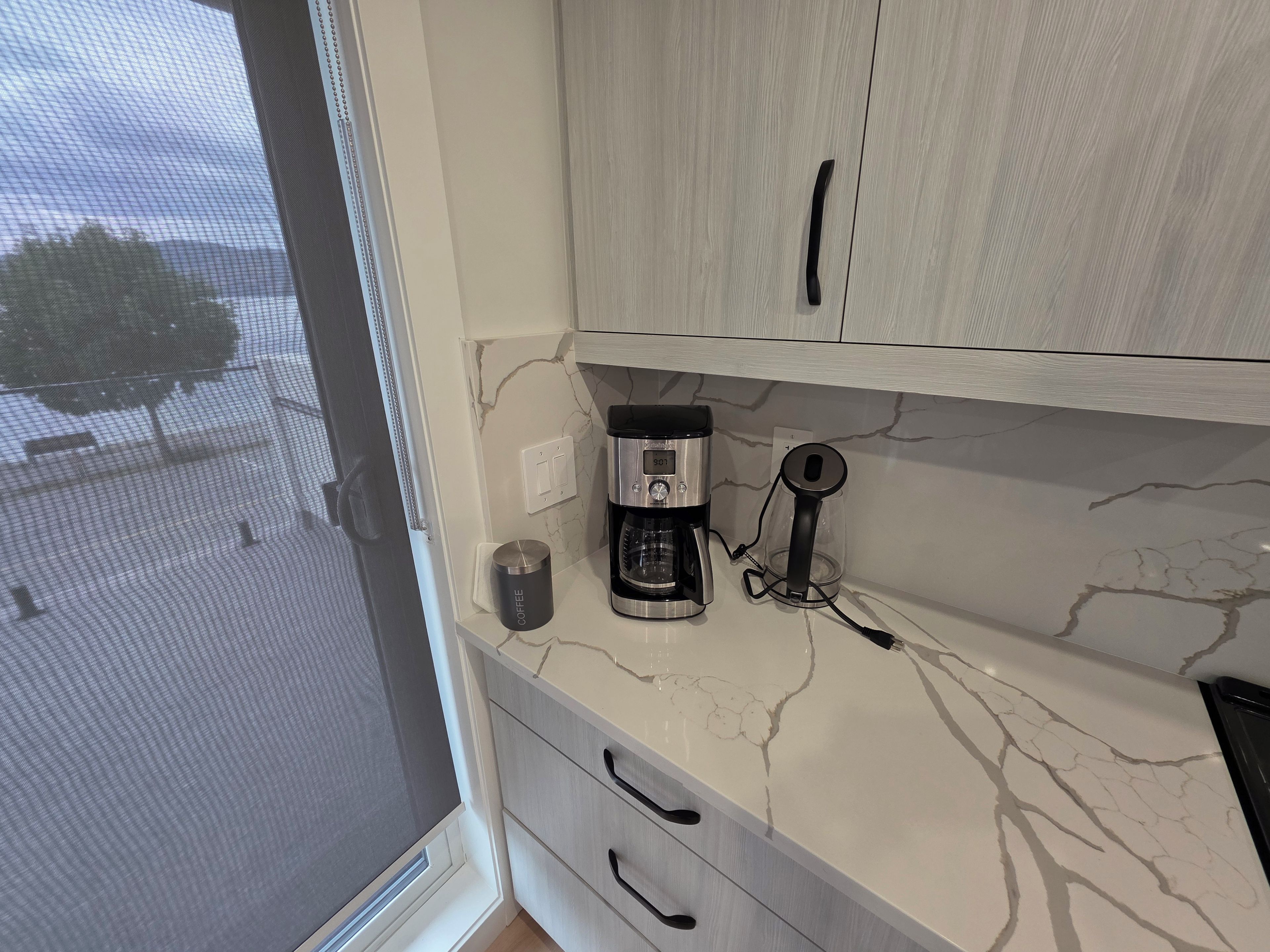 Cozinha com cafeteira, xícara e armário.