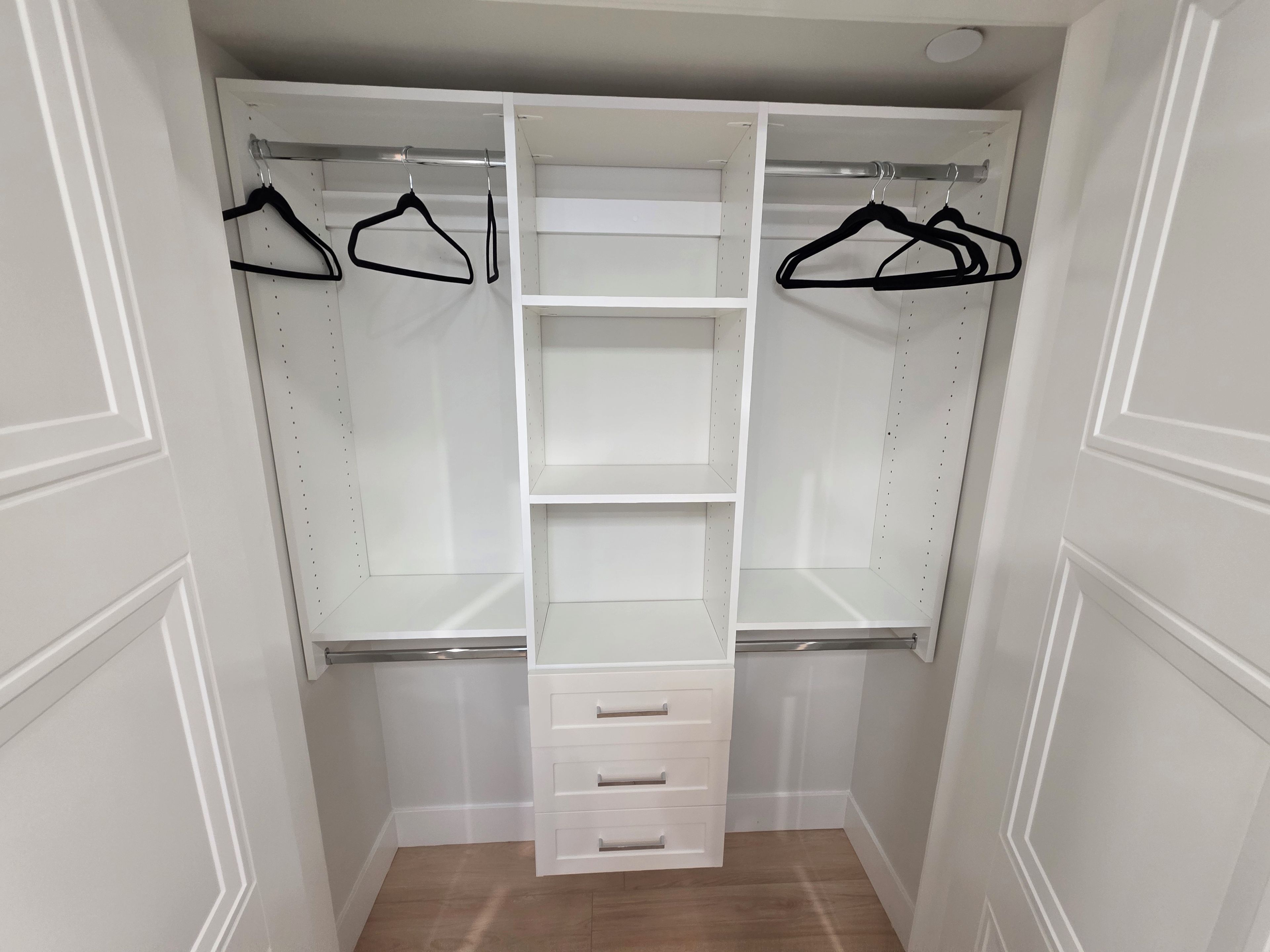 A walk-in closet with open shelves, hanging space, and a central drawer unit.