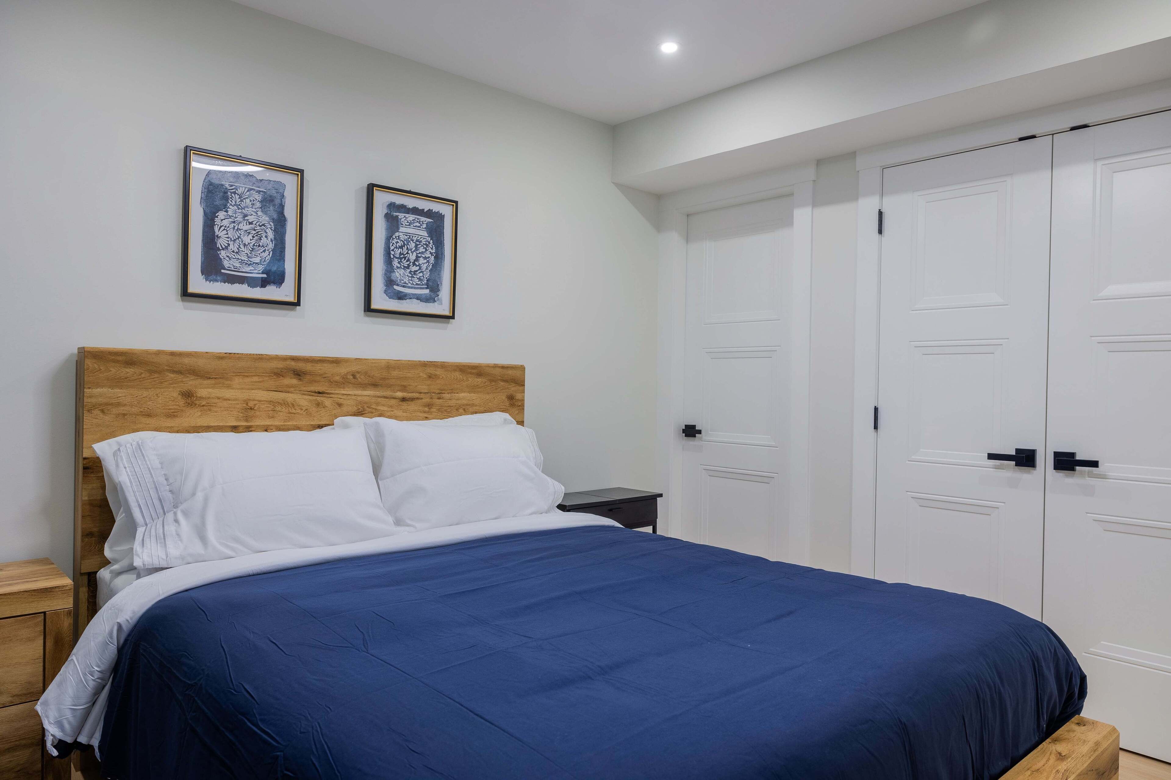 A bedroom with a wooden headboard, a blue bedspread, white pillows, and two framed artworks on the wall.