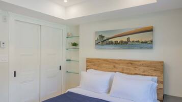 A bedroom with a bed, white walls, a wooden headboard, a painting of a bridge, and a closet with glass shelves.