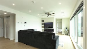 Uma sala de estar moderna com um sofá cinza escuro, uma TV de tela plana e um ventilador de teto.