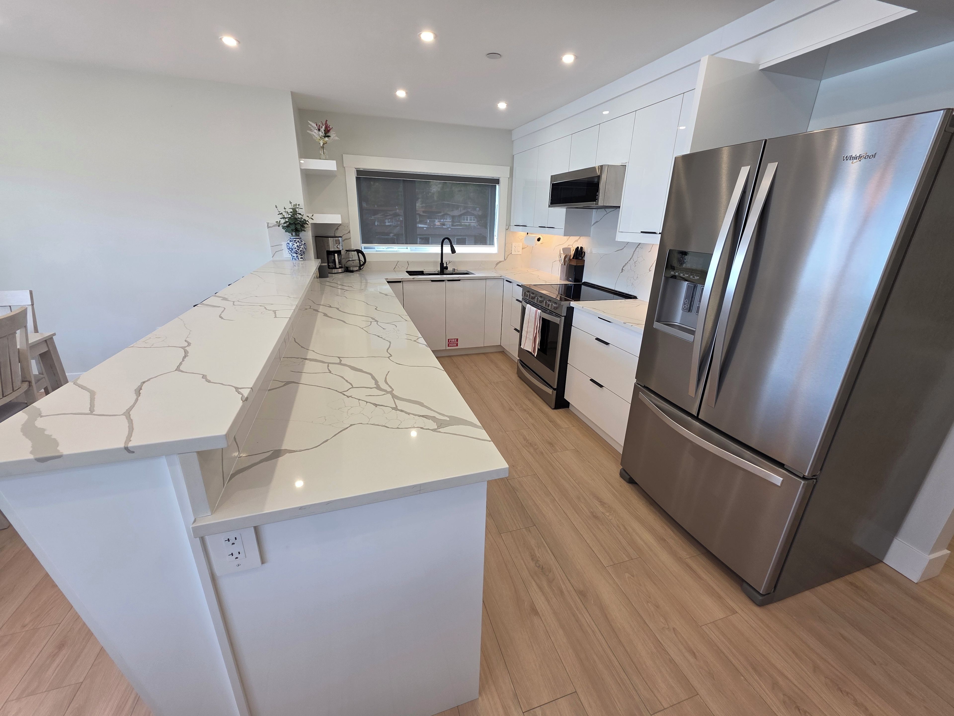 Een moderne keuken met een marmeren aanrecht, roestvrijstalen apparatuur en houten vloeren.