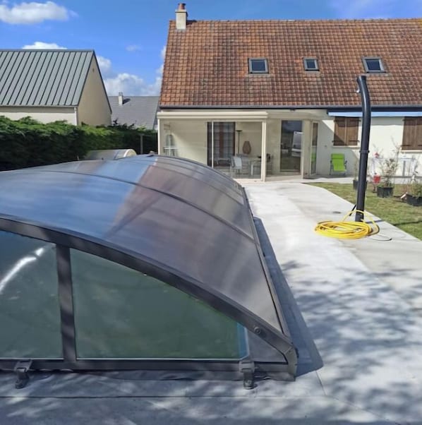 A modern house with a curved glass extension, a visible chimney, and a clear sky.