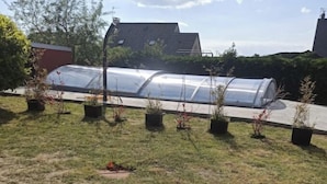 A greenhouse structure with transparent walls, surrounded by potted plants on a grassy area.