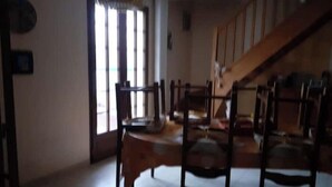 A dining area with wooden chairs and a table, a staircase, and a window with vertical blinds.