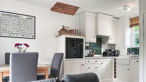 A modern kitchen with white cabinets, a dining table with chairs, and a grey sofa.