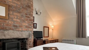 A bedroom with a brick fireplace, a flat-screen TV, a bedside table, and a bed with a white comforter.