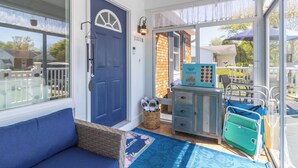 Une véranda baignée de lumière, avec une porte bleue, un panier en osier et un canapé bleu.