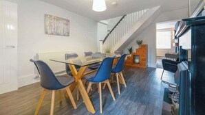 Een moderne eetruimte met een glazen tafel, blauwe stoelen, een houten vloer, een trap en een zwarte kast.