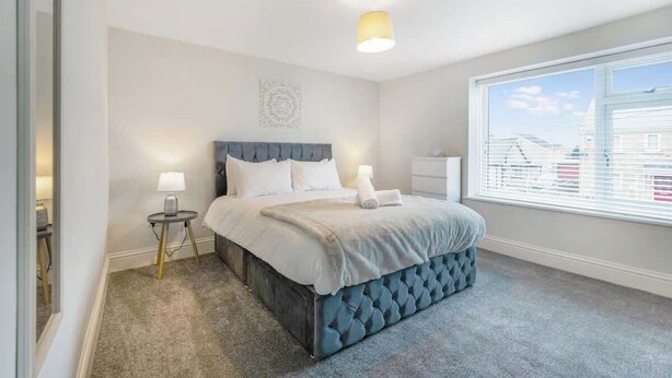 Een slaapkamer met een bed, nachtkastjes, een raam met zonwering en uitzicht op gebouwen.