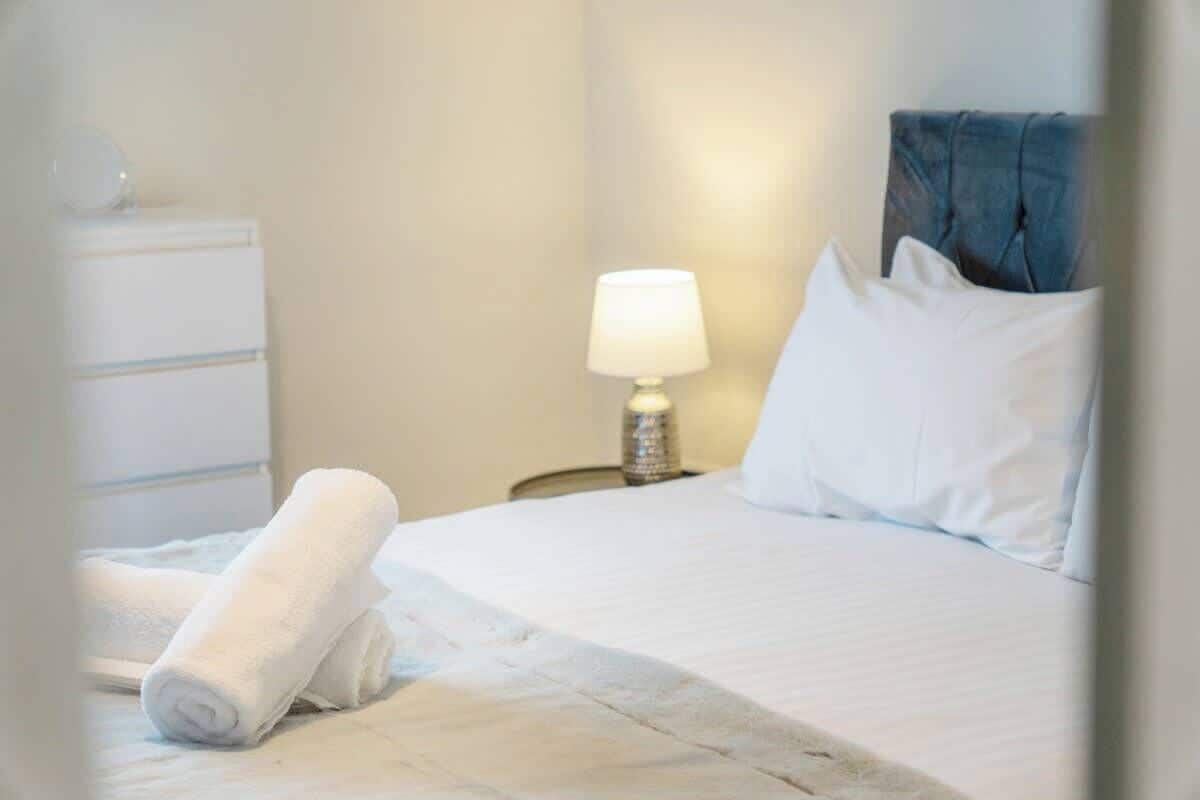 A neatly made bed with white linens, a bedside lamp, and a blue headboard.
