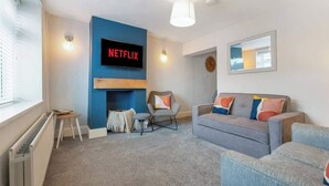 Een moderne woonkamer met een blauwe accentmuur, een open haard, een grijze bank en een flatscreen televisie waarop 'NETFLIX' staat.