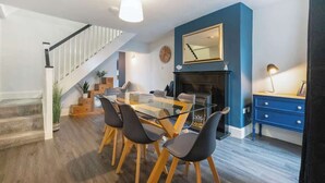 Een eethoek met een glazen tafel, zwarte stoelen, een blauwe accentmuur, een open haard en een trap.