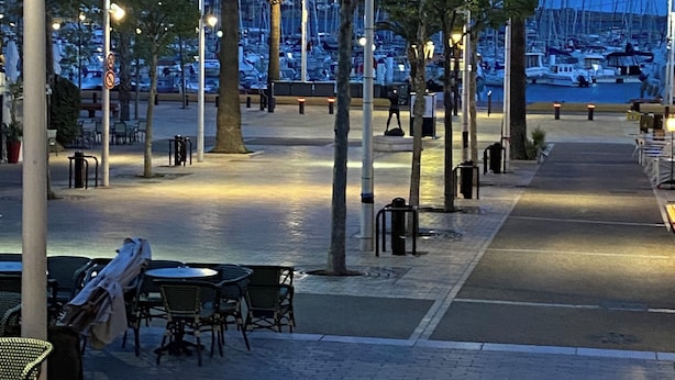 A paved walkway with tables and chairs, palm trees, and a marina with boats in the background. - Magnifique 6 Personnes Avec Terasse Tropezienne Refait à Neuf (Bandol)