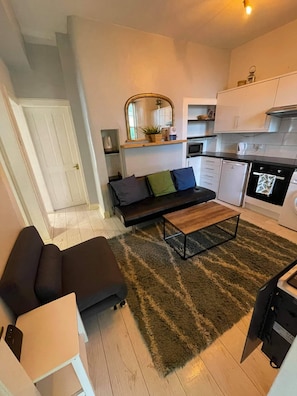 A compact living space with a sofa, a coffee table, a kitchen area, and a small dining table. - Unique two bed Main Door Flat at the Meadows (Edinburgh)