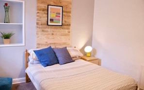 A neatly made bed with blue and white bedding, a bedside lamp, and a wall-mounted shelf with a plant and a vase. - Unique two bed Main Door Flat at the Meadows (Edinburgh)